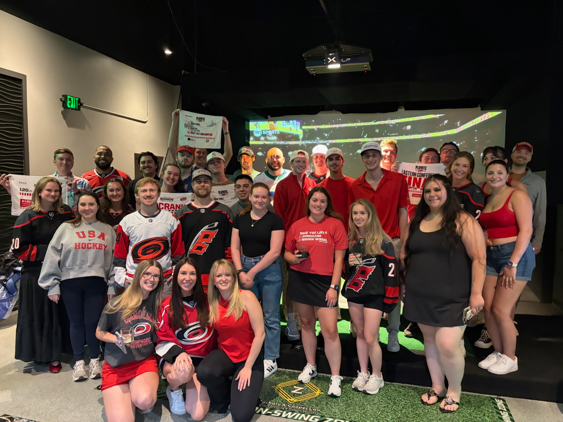 Big group in Canes jerseys at the golf simulator watch party